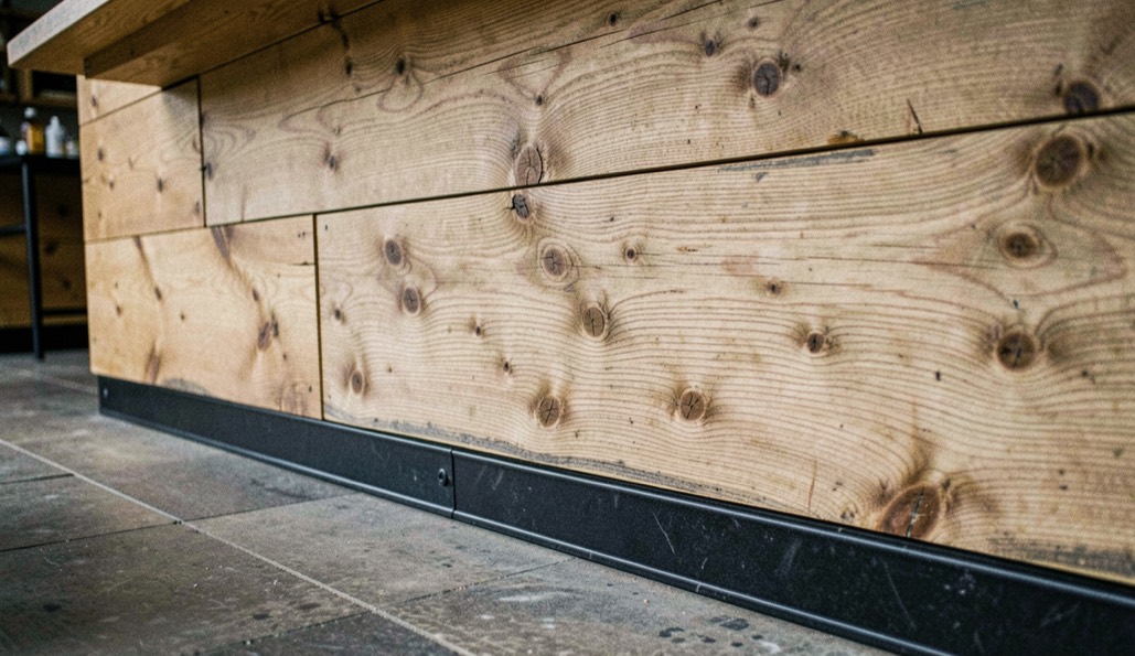 Barfront van verweerde eiken planken met zichtbare noesten, een blad van dik hout en een zwart stalen voetrail